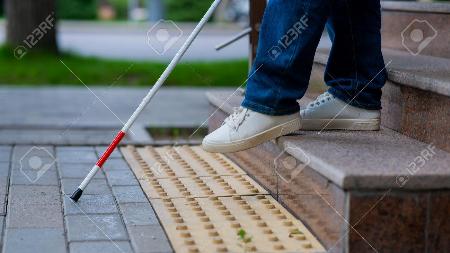 Close-up of female foot, walking stick and tactile tiles. Blind woman walking down stairs using a cane.